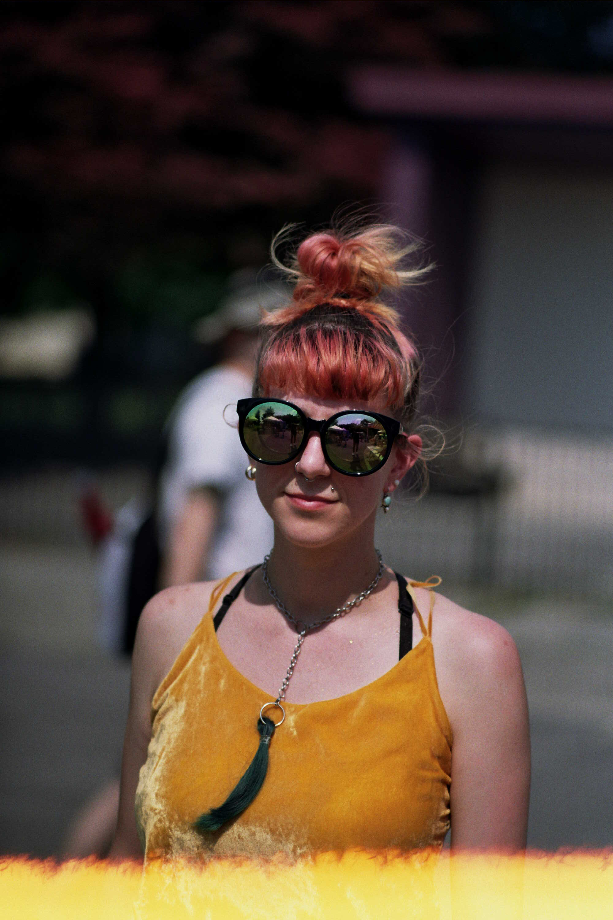 A person with a bright yellow shirt, pink hair, and enormous sunglasses looks at the camera.