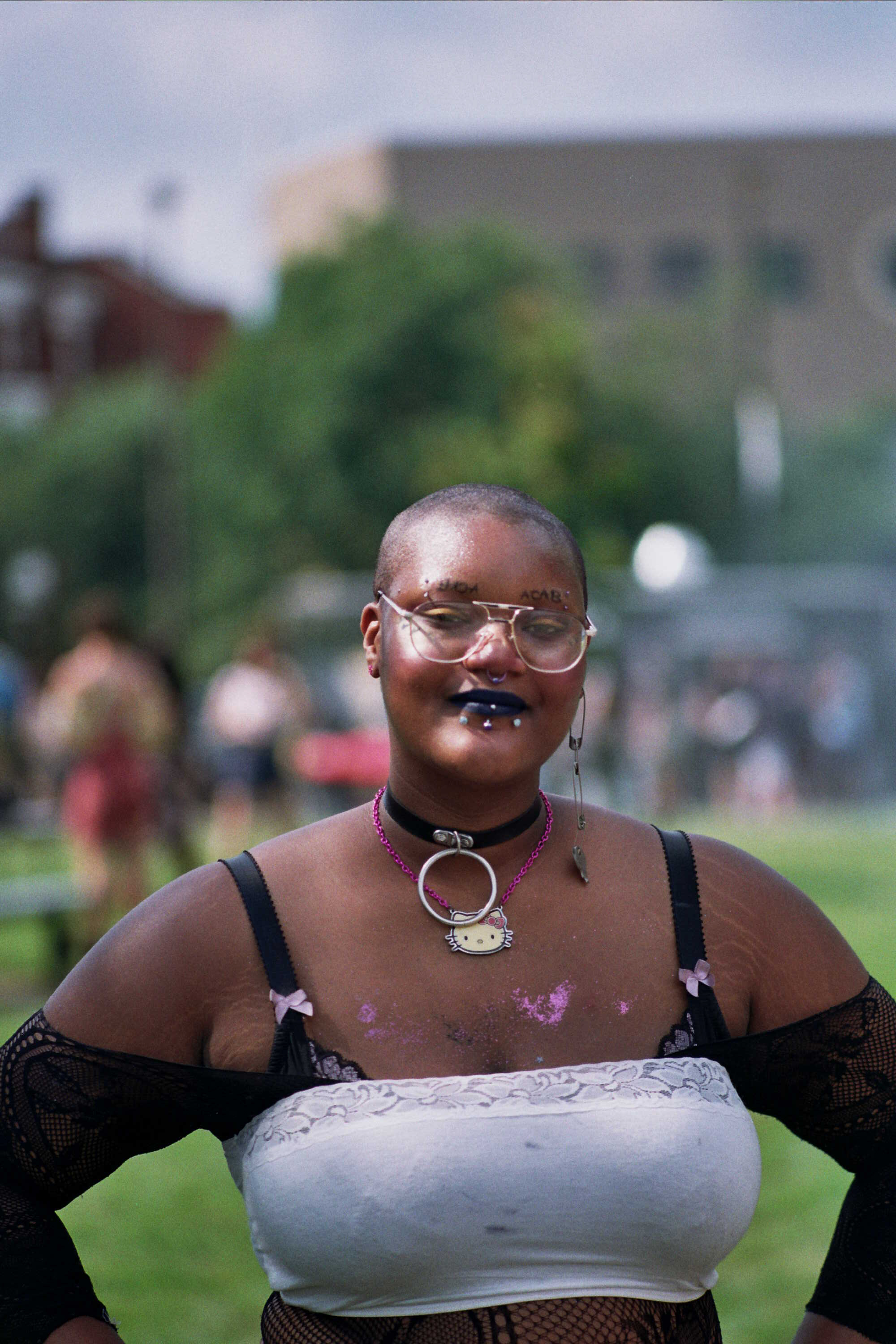 A person with a shaved head, glasses, and a Hello Kitty leather collar looks into the camera.