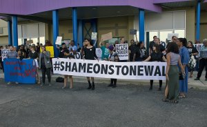 A crowd of protesters hold a large white banner with black texts that reads "#ShameOnStonewall."