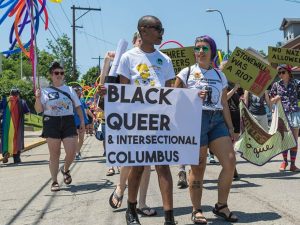 A colorful protest march led by two activists carrying a "Black Queer & Intersectional Columbus" sign.